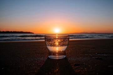 Refreshing glass of water against a sunset beach