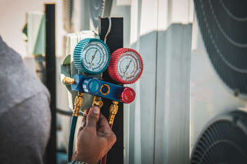 Air conditioning, HVAC service technician using gauges to check refrigerant and add refrigerant.	