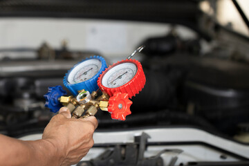Auto mechanic using a gauge to check refrigerant and refill car air conditioning.