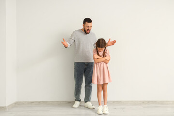 Angry father shouting at his daughter near light wall. Domestic violence concept