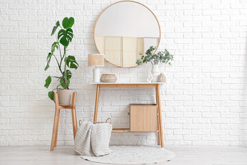 Table with decor, houseplant and mirror on white brick wall in room