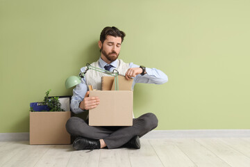 Fired young man with boxes of personal stuff sitting near green wall