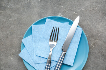 Plate with cutlery and blue paper napkins on grey grunge background