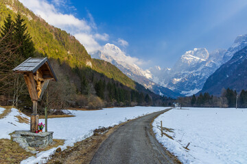 Wooden wayside cross overlooking snowy Log pod Mangartom valley in Slovenia