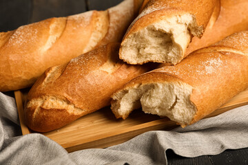Tray with fresh baguettes on black wooden background, closeup