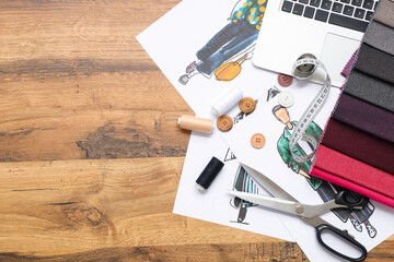Laptop with drawings and sewing supplies on wooden background