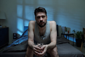 Portrait of Caucasian young adult holding glass of water looking into camera with serious...