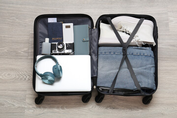 Open suitcase with clothes and modern gadgets on grey wooden floor