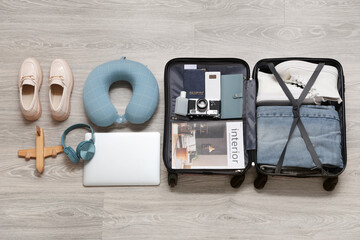 Suitcase with travel accessories and modern gadgets on grey wooden floor
