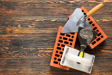Trowel with cement, plastering float and bricks on wooden background