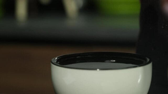 Woman uses pair of teaspoons to skim off excess liquid from top of mug. Barista casts coffee shaking spoons in basin of water slow motion