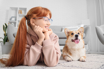 Teenage redhead girl with cute Corgi dog lying on carpet at home