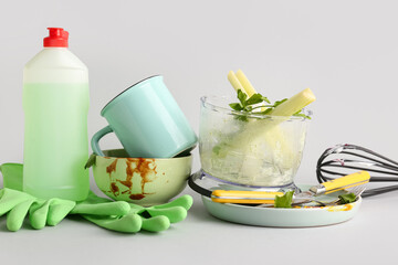 Many dirty dishes with cutlery, rubber gloves and detergent on grey background