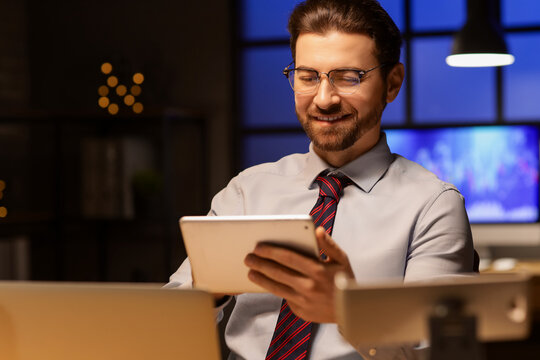 Handsome businessman working with tablet computer in office at night