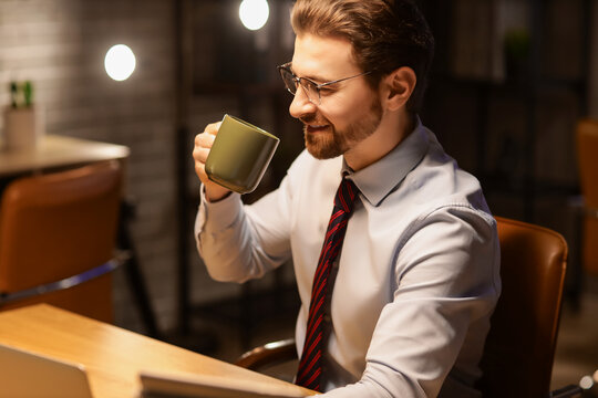 Handsome businessman with coffee and laptop working in office at night
