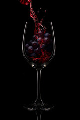 Red wine pouring over fresh grapes in a wine glass, isolated on black