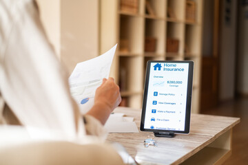 Woman reviewing home insurance policy documents and managing coverage on a digital tablet,...