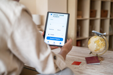 Woman using travel app on digital tablet for booking flight, searching flights and planning travel with globe, passport and credit card on table