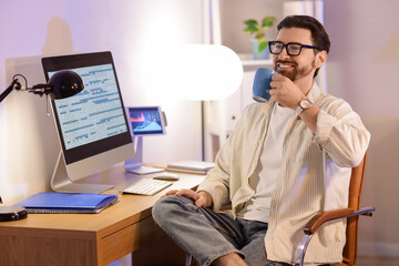 Handsome programmer with cup of coffee sitting at office in evening
