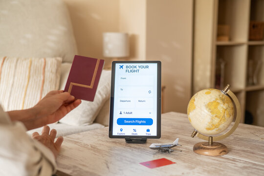 Traveler holding passport is booking a flight using a travel app on a tablet, with a globe and a miniature airplane on the table, symbolizing wanderlust and online travel planning