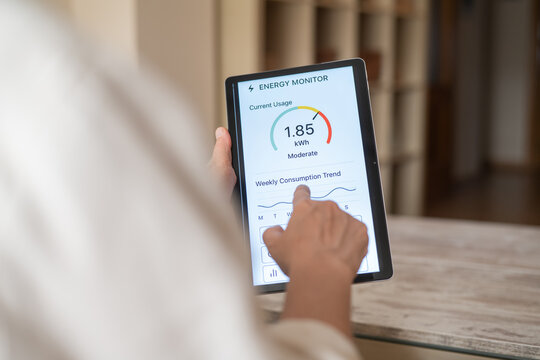Person is using a tablet with an energy monitor app to track their weekly energy consumption and identify trends, promoting energy efficiency and cost savings