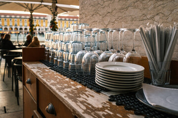 Stacked glassware and plates at outdoor cafe counter in afternoon