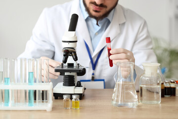 Male scientist with test tube and microscope working in laboratory, closeup