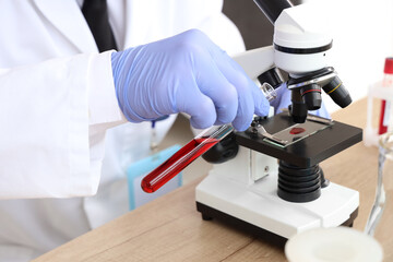 Male scientist with blood sample and microscope working in laboratory, closeup