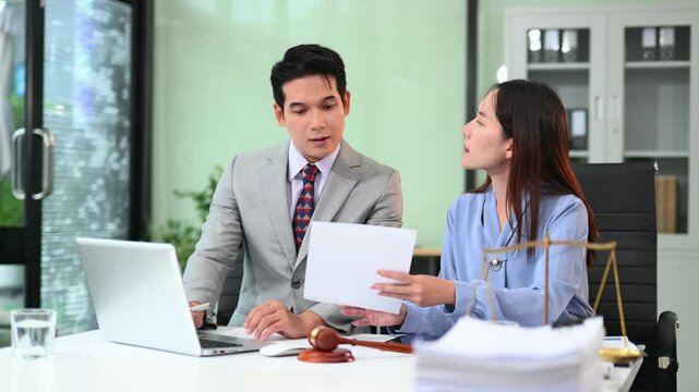 Asian lawyers and clients discuss legal matters and contracts with laptops and paperwork in a modern office.