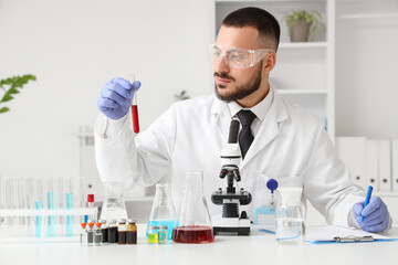Fototapeta premium Male scientist with blood sample and microscope working in laboratory