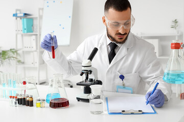 Male scientist with blood sample and microscope working in laboratory
