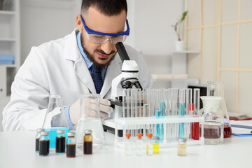 Male scientist with safety goggles looking through microscope in laboratory
