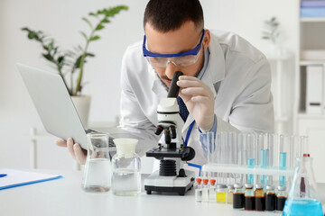 Male scientist with laptop looking through microscope in laboratory