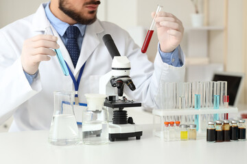 Male scientist with test tubes and microscope at table in laboratory, closeup