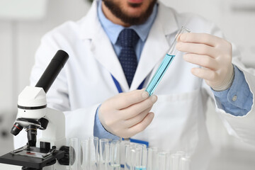 Male scientist with test tube and microscope in laboratory, closeup