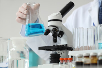 Male scientist with flask and microscope at table in laboratory, closeup