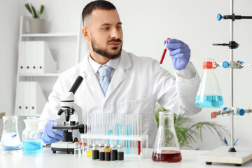 Male scientist with blood sample and microscope working in laboratory