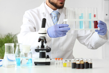 Male scientist with test tubes and microscope at table in laboratory, closeup