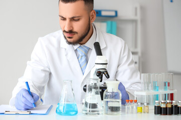 Fototapeta premium Male scientist with microscope writing at table in laboratory