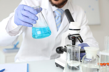 Male scientist with flask and microscope at table in laboratory, closeup