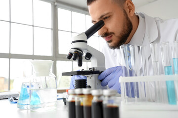 Male scientist looking through microscope at table in laboratory, closeup