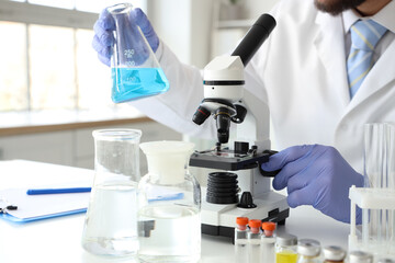 Male scientist with flask and microscope at table in laboratory, closeup