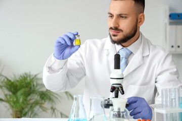 Male scientist with ampule and microscope working in laboratory