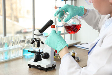 Female scientist pouring liquid from flask into test tube in laboratory, closeup