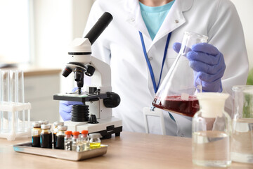 Female scientist with flask and microscope at table in laboratory, closeup