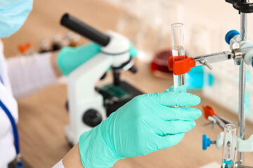 Female scientist with test tube and microscope working in laboratory, closeup