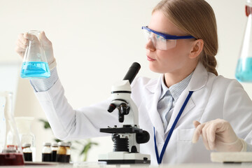 Female scientist with flask and microscope working in laboratory