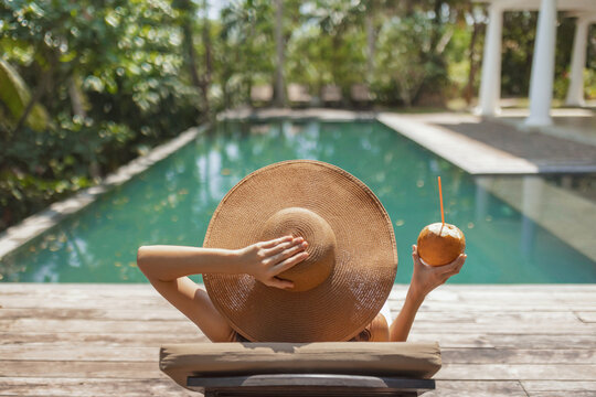 Woman Relaxing by Pool with Sun Hat and Coconut