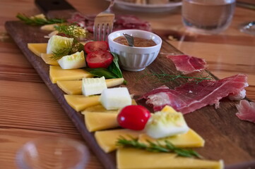 Wooden plate with prosciutto, cheese, spread, tomato and herbs