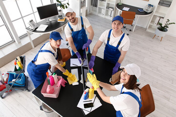 Team of young janitors cleaning desk in office, top view